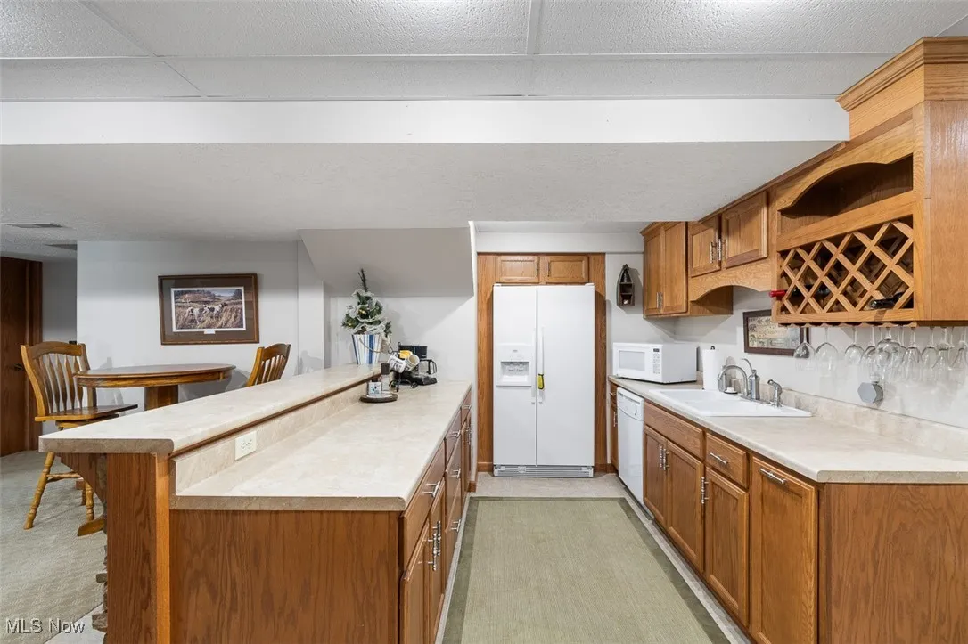 Kitchen with brown cabinets, white appliances, light countertops, a kitchen bar, and light carpet