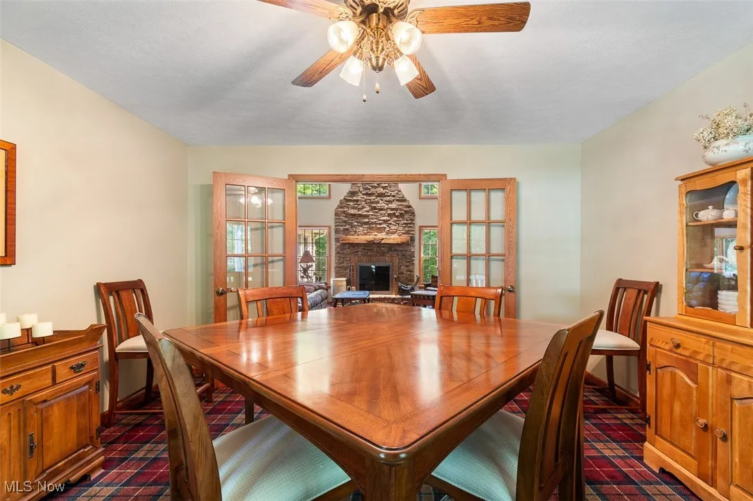 Dining room featuring a fireplace, ceiling fan, french doors, and a textured ceiling