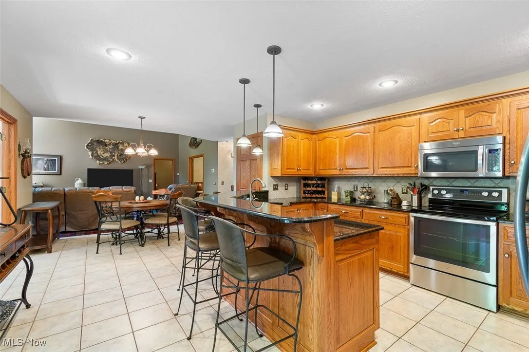 Kitchen featuring stainless steel appliances, a chandelier, light tile patterned flooring, decorative backsplash, and a breakfast bar