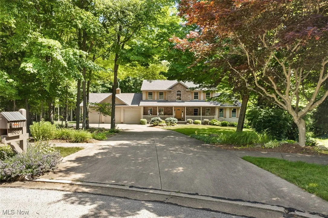 View of front facade with covered porch, concrete driveway, a chimney, and view of wooded area