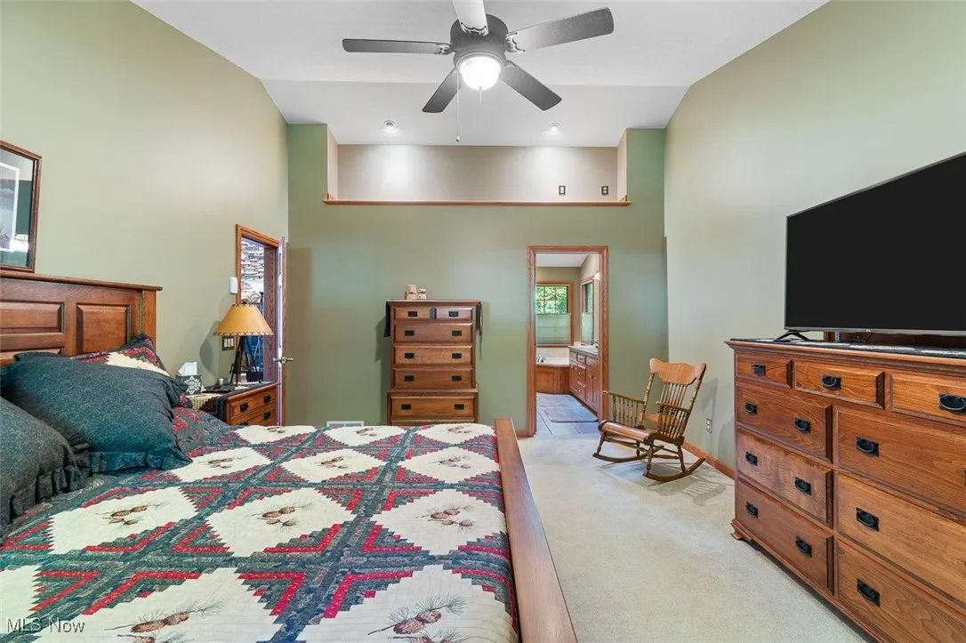 Bedroom featuring light carpet, ensuite bath, ceiling fan, and high vaulted ceiling