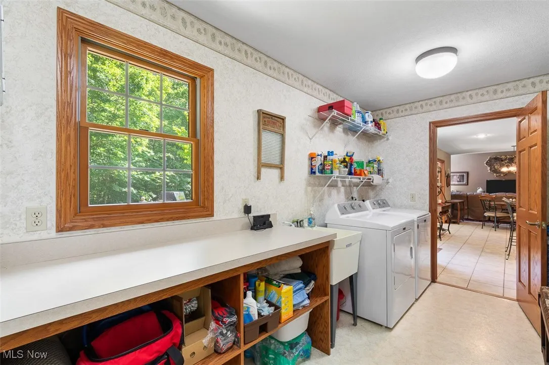 Washroom featuring a desk, washing machine and dryer, and wallpapered walls