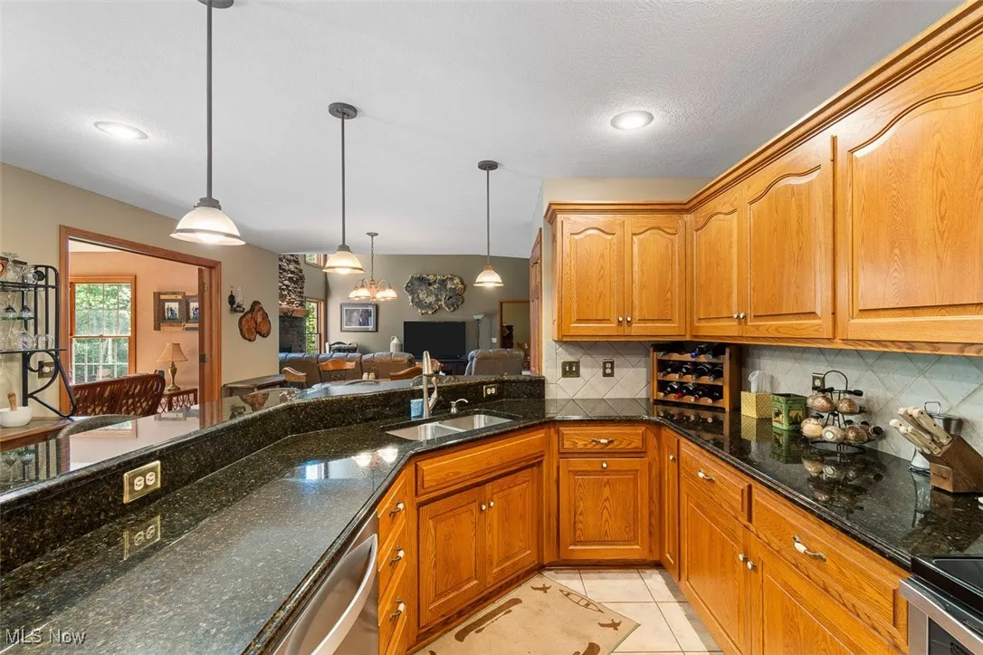 Kitchen featuring dark stone countertops, decorative backsplash, light tile patterned floors, and hanging light fixtures