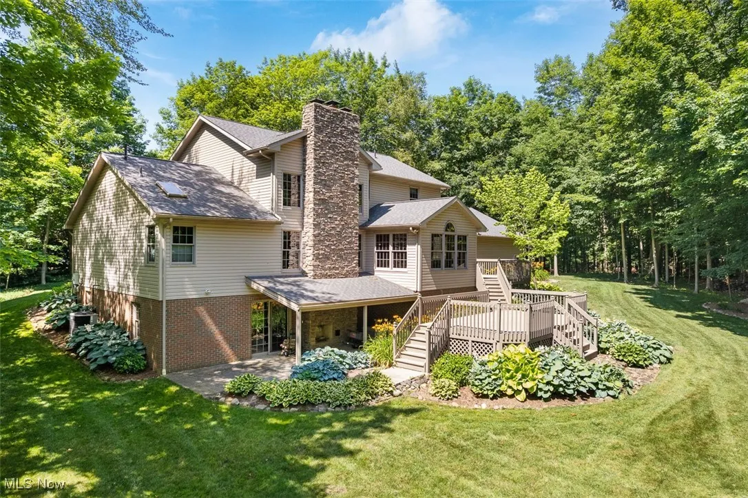 Back of house featuring a patio, a lawn, a chimney, a wooden deck, and stairs