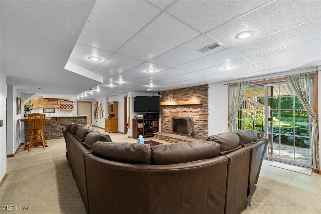 Living area with a stone fireplace, light colored carpet, a paneled ceiling, and bar