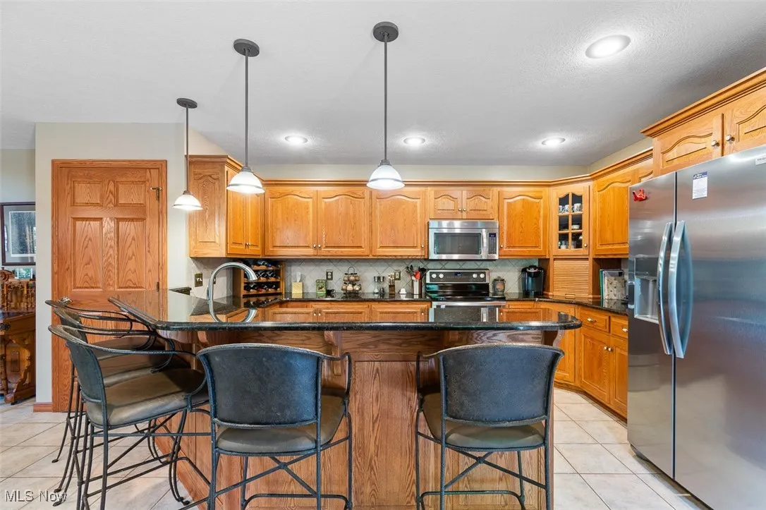 Kitchen with a breakfast bar area, appliances with stainless steel finishes, dark stone counters, light tile patterned floors, and recessed lighting