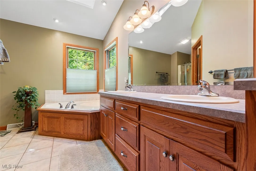 Full bath featuring light tile patterned floors, a skylight, double vanity, a garden tub, and a stall shower