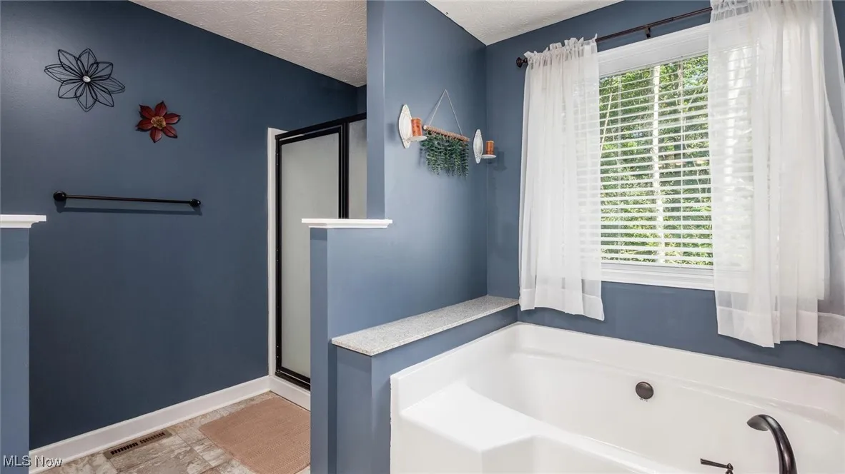 Full bathroom with a soaking tub with jets, a stall shower, and a textured ceiling
