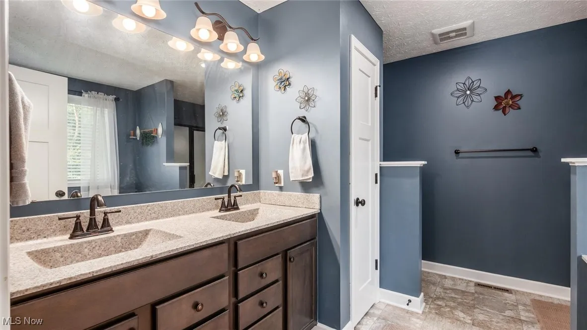 Bathroom featuring a textured ceiling, double vanity, and light stone finish flooring
