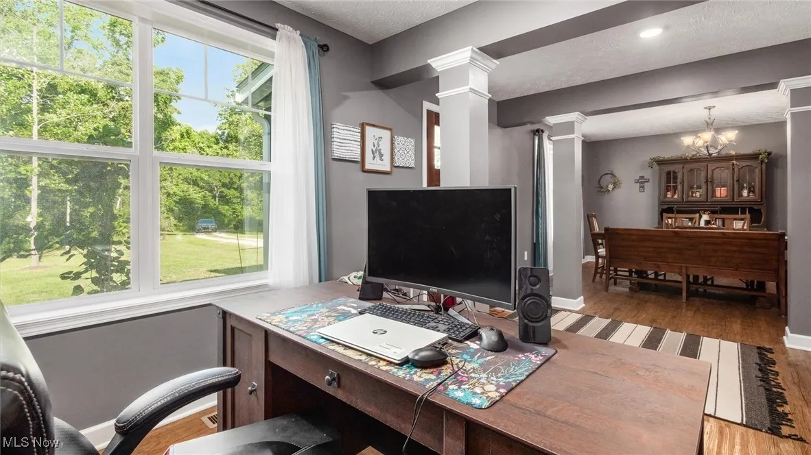 Office with a textured ceiling, light wood-style floors, a chandelier, and decorative columns