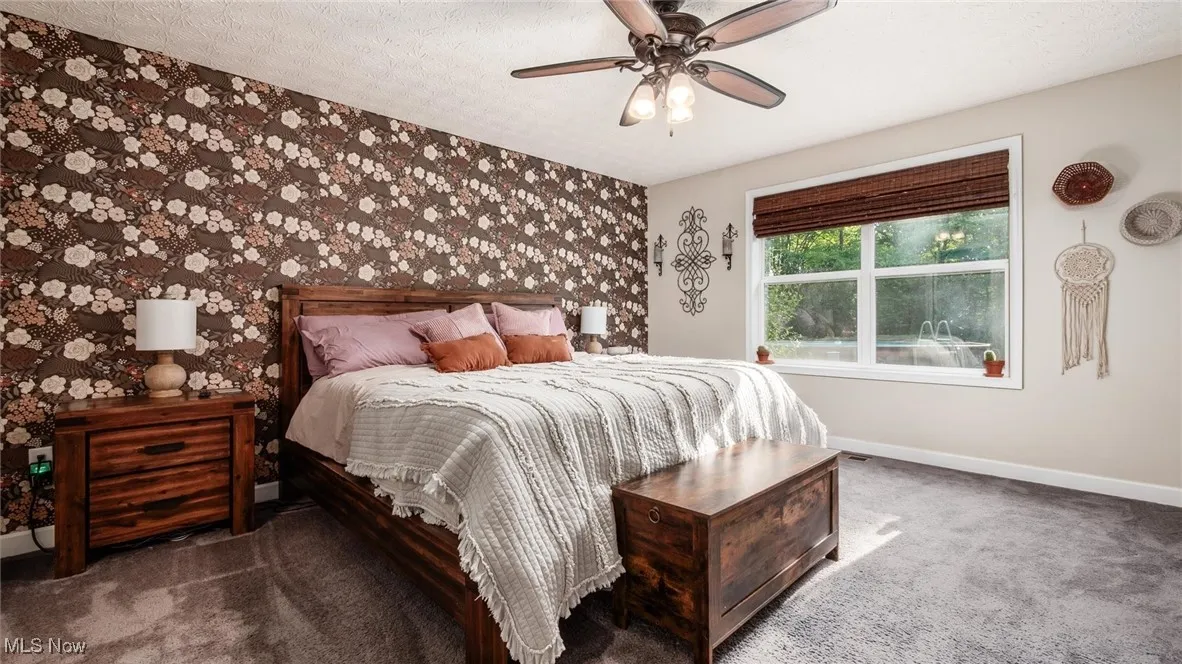 Carpeted bedroom with wallpapered walls, an accent wall, a ceiling fan, and a textured ceiling