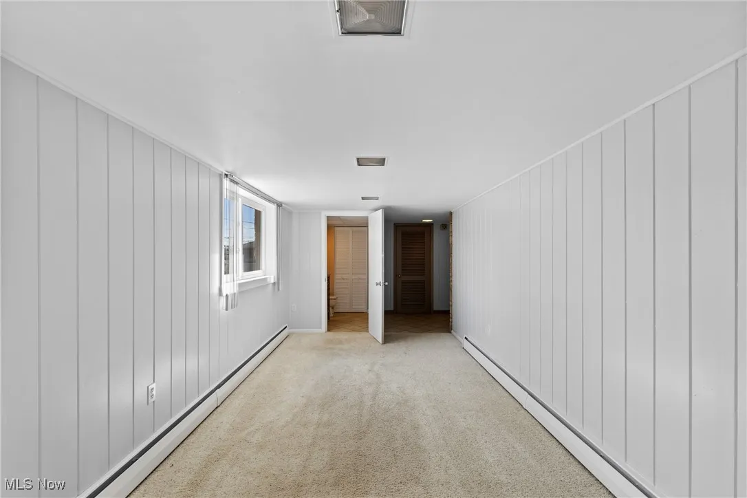 Hallway featuring a baseboard heating unit, wooden walls, and carpet floors