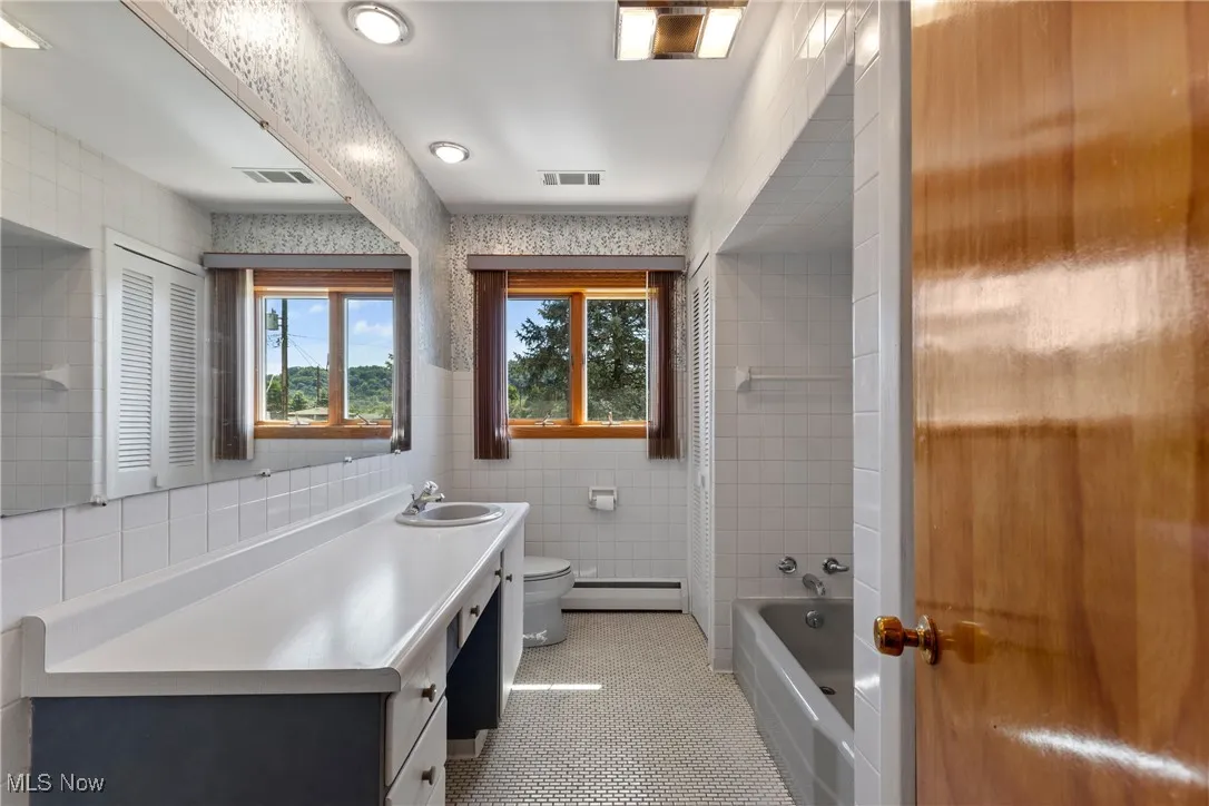 Full bathroom featuring tile walls, shower / bath combination with curtain, vanity, light tile patterned floors, and a baseboard heating unit
