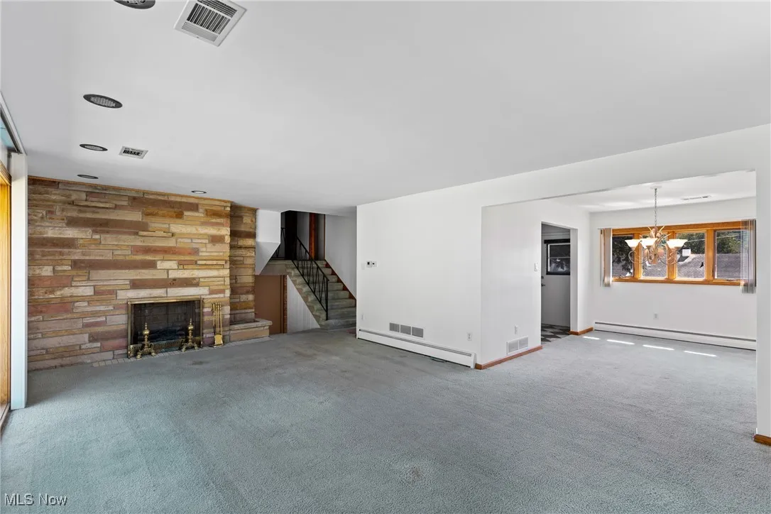Unfurnished living room featuring a fireplace, carpet flooring, baseboard heating, and a chandelier