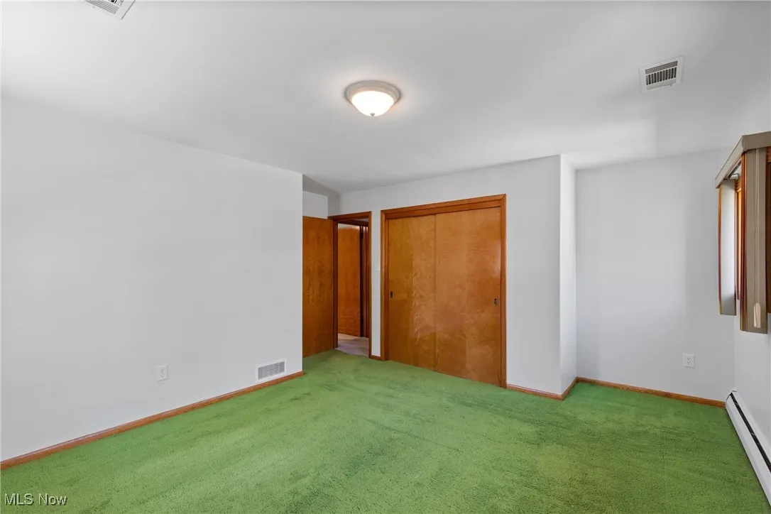 Unfurnished bedroom with a baseboard heating unit, carpet, and a closet
