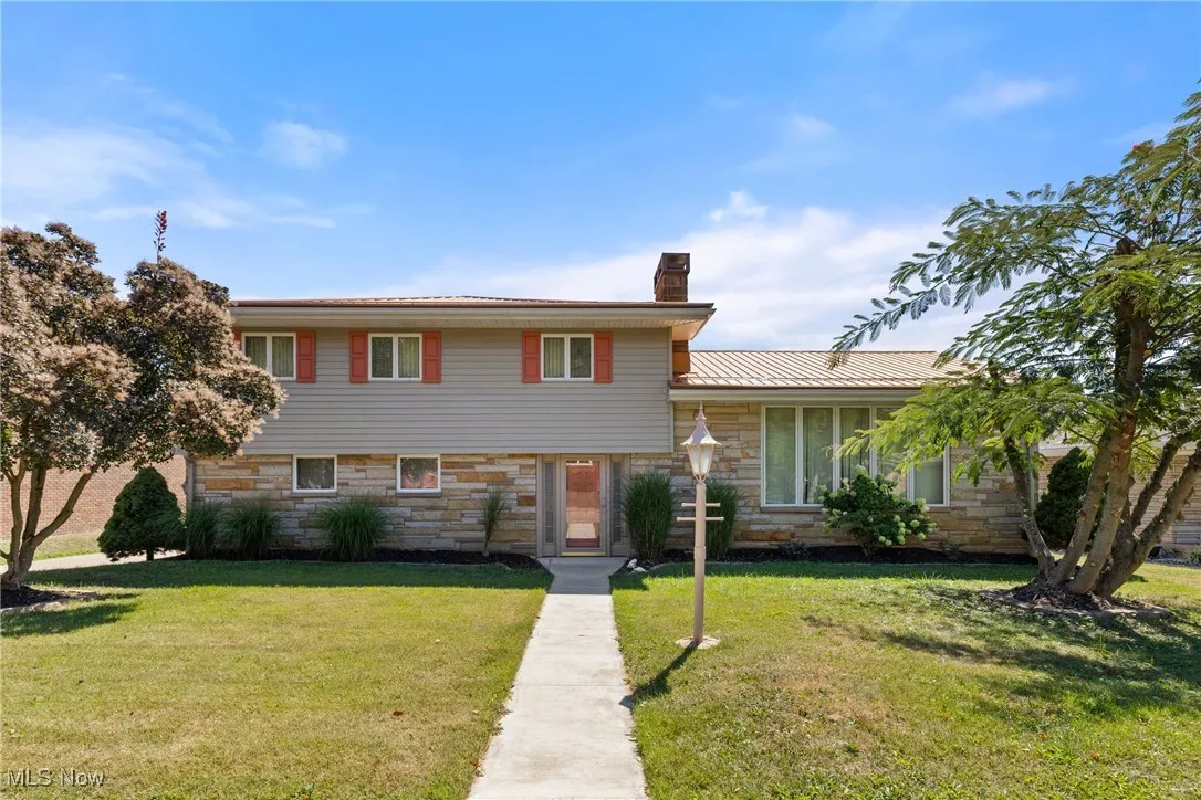 Split level home with stone siding, a front lawn, a chimney, and a metal roof