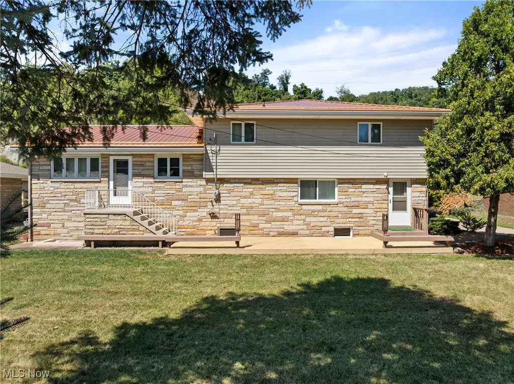 Back of house with stone siding, a yard, and a patio