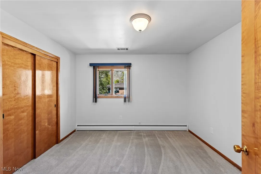 Unfurnished bedroom featuring light carpet, a closet, and baseboard heating