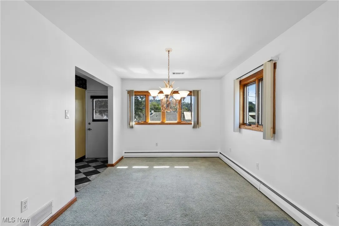 Unfurnished dining area featuring baseboard heating, a chandelier, and carpet flooring