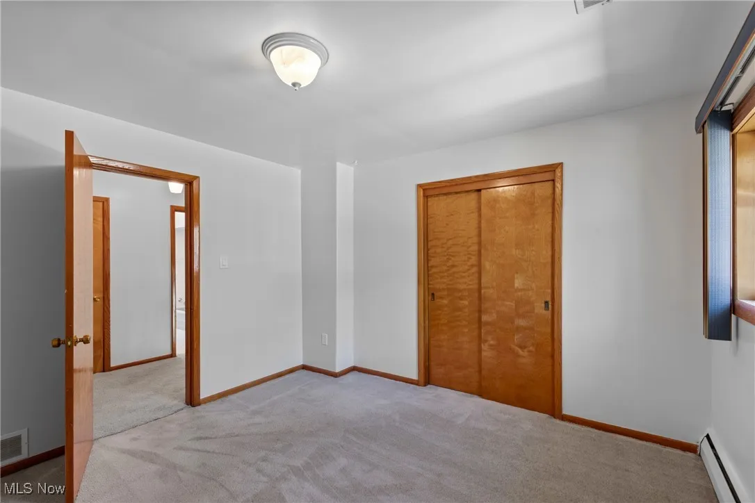 Unfurnished bedroom featuring baseboard heating, carpet flooring, and a closet