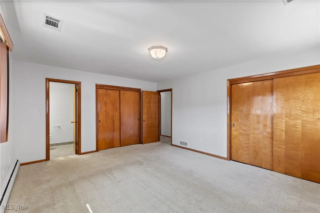 Unfurnished bedroom featuring baseboard heating, carpet floors, multiple closets, and ensuite bath