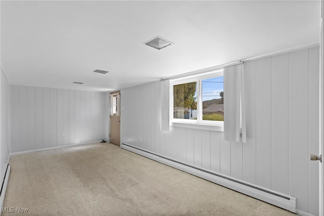 Carpeted spare room featuring a baseboard radiator and wooden walls