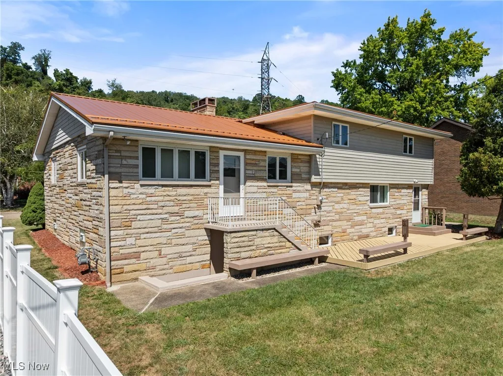 Back of house featuring stone siding, a chimney, a metal roof, and a wooden deck
