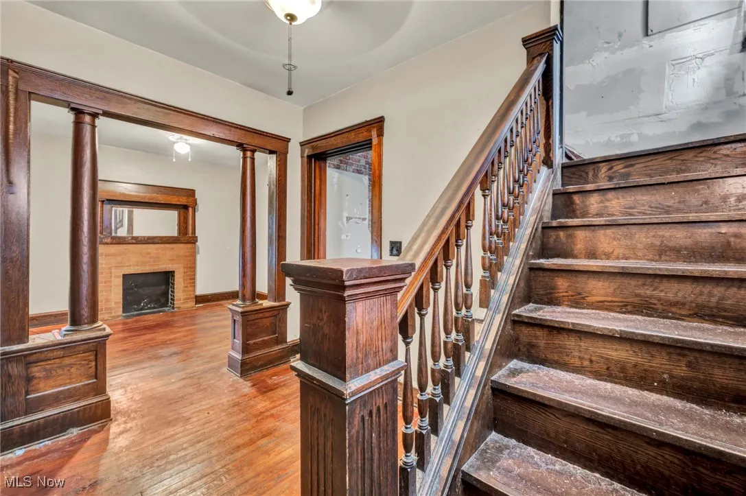 Staircase with hardwood / wood-style floors, decorative columns, and a fireplace