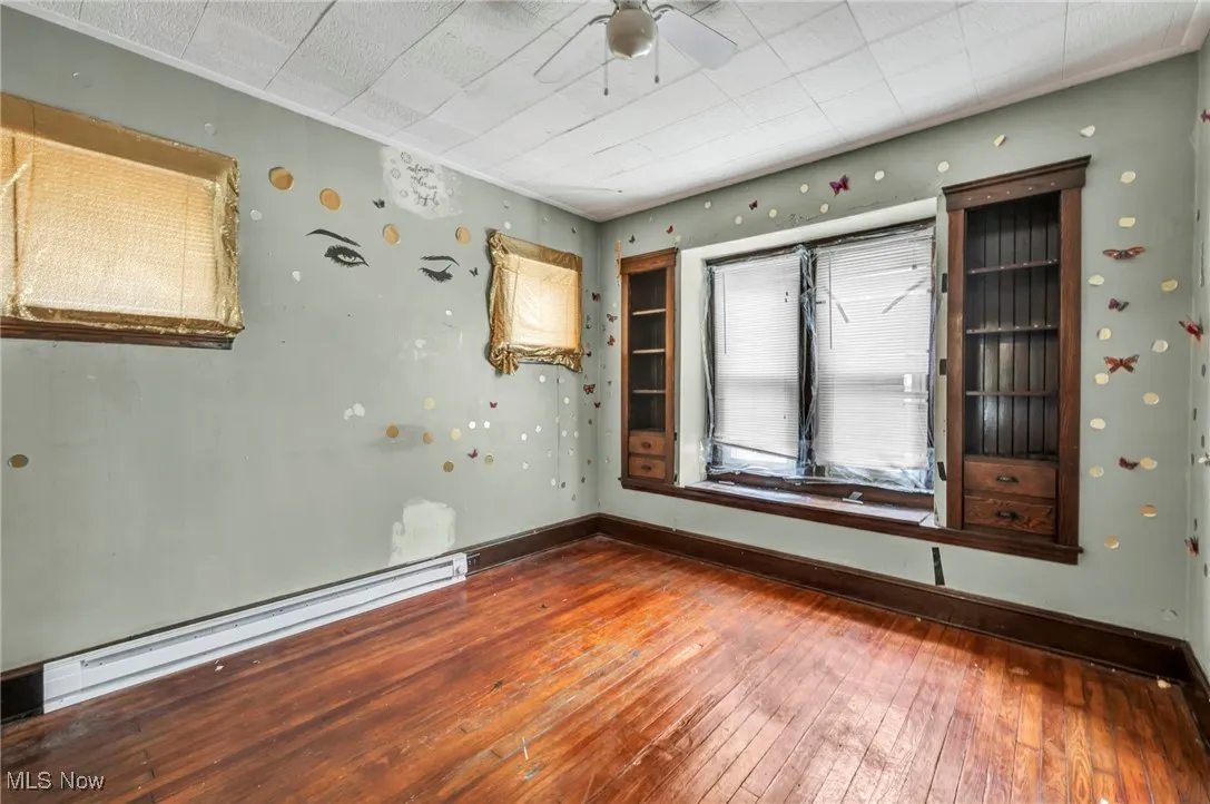 Spare room featuring hardwood / wood-style flooring, a baseboard heating unit, and a ceiling fan