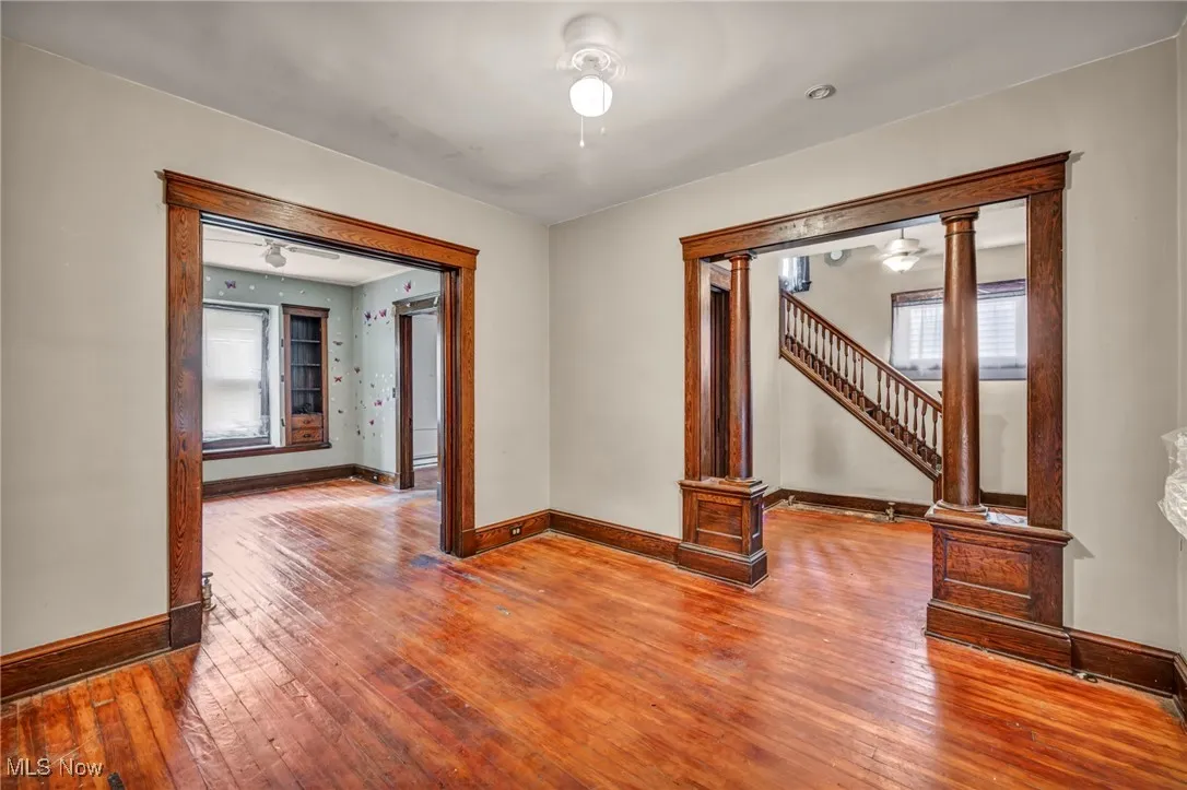 Empty room featuring hardwood / wood-style floors, ornate columns, a ceiling fan, and stairs
