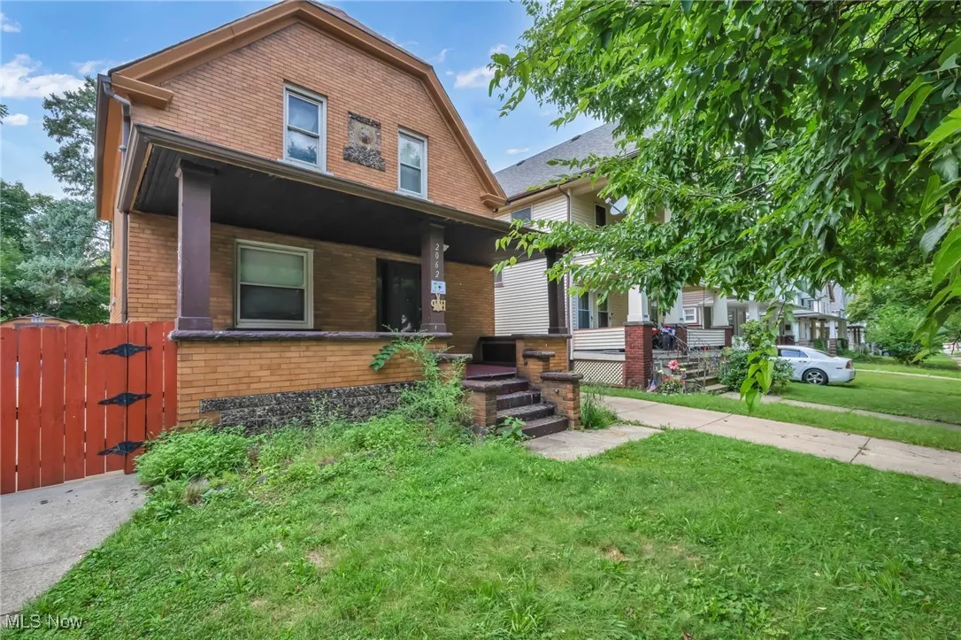 Dutch colonial with brick siding, a gate, a front lawn, and a porch