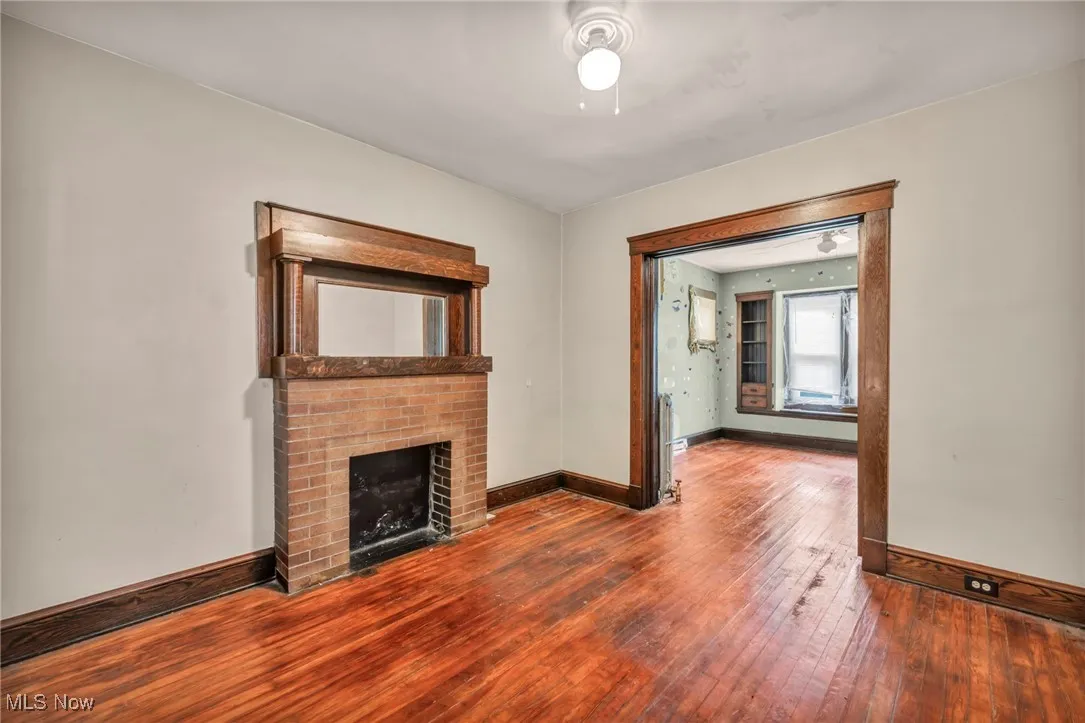 Unfurnished living room featuring wood-type flooring and a brick fireplace