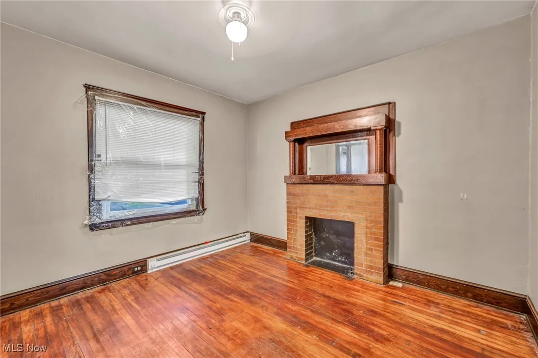 Unfurnished living room with baseboard heating, wood-type flooring, and a fireplace