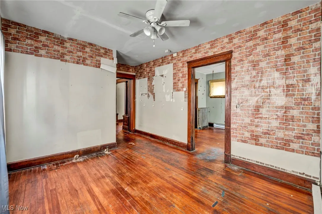 Unfurnished room with brick wall, hardwood / wood-style floors, ceiling fan, and a baseboard radiator