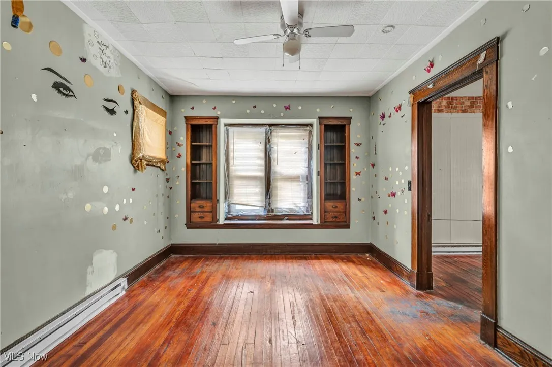 Unfurnished room featuring hardwood / wood-style flooring, a baseboard heating unit, wallpapered walls, and ceiling fan