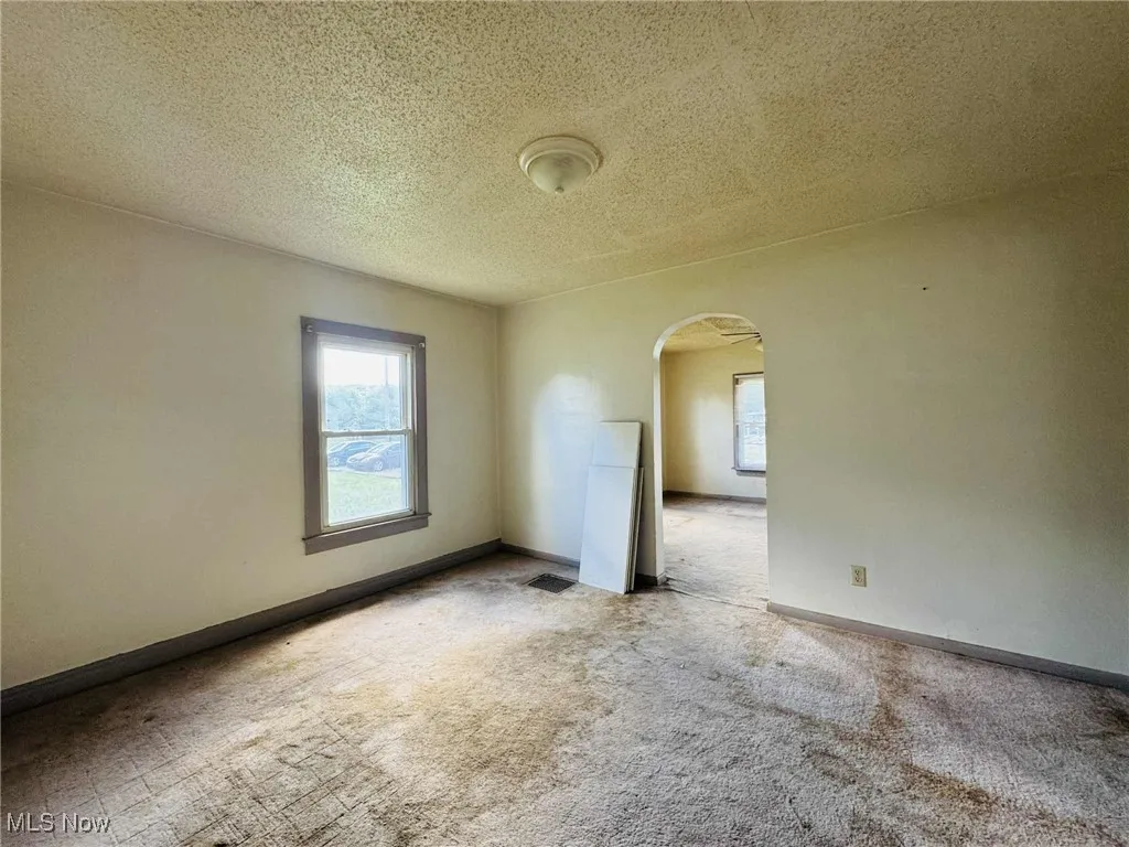 Empty room featuring arched walkways, a textured ceiling, and carpet