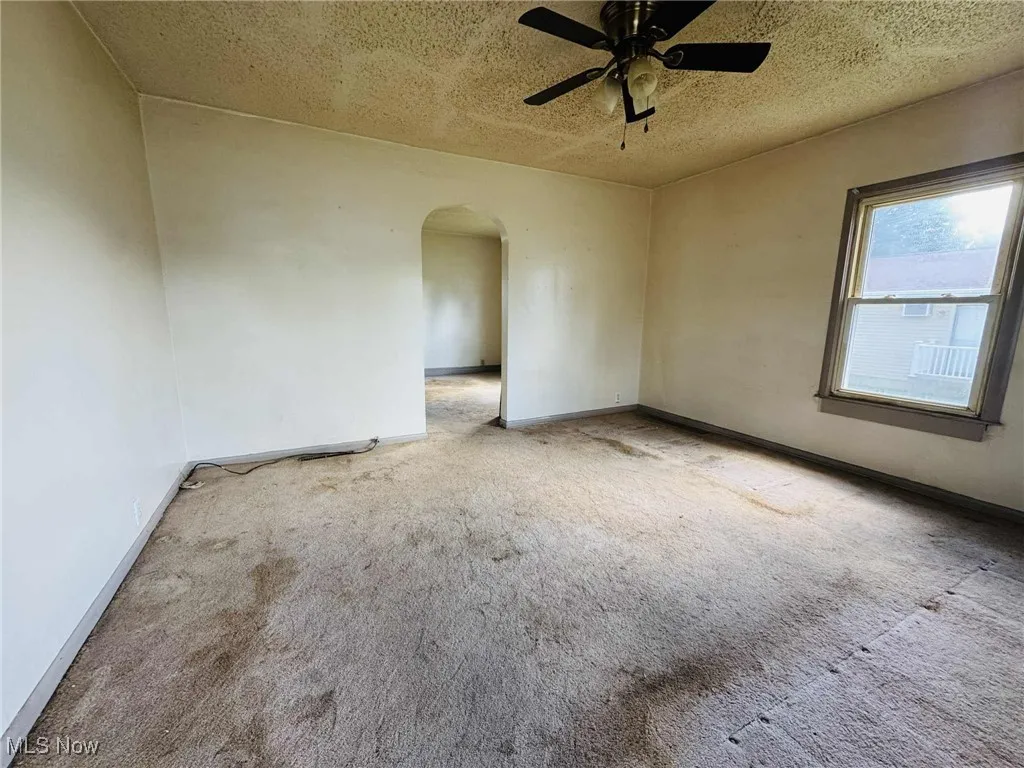 Empty room with arched walkways, a textured ceiling, carpet flooring, and ceiling fan