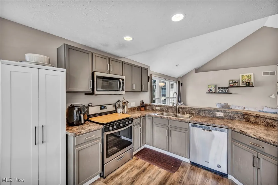 Kitchen with gray cabinets, appliances with stainless steel finishes, vaulted ceiling, and a textured ceiling