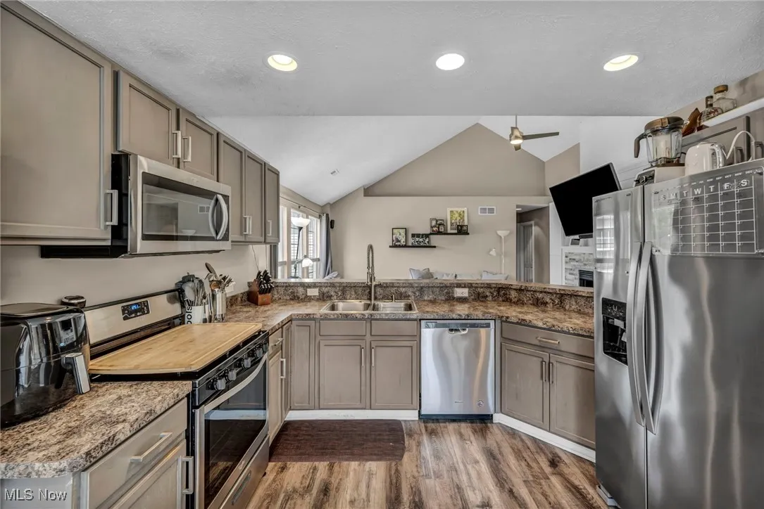 Kitchen with vaulted ceiling, stainless steel appliances, light wood-style floors, gray cabinetry, and recessed lighting