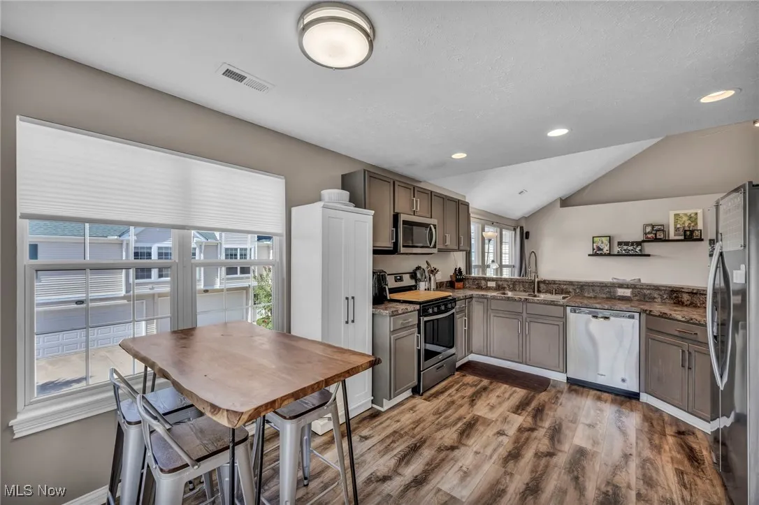Kitchen with appliances with stainless steel finishes, lofted ceiling,  recessed lighting, and dark stone countertops
opens into living space