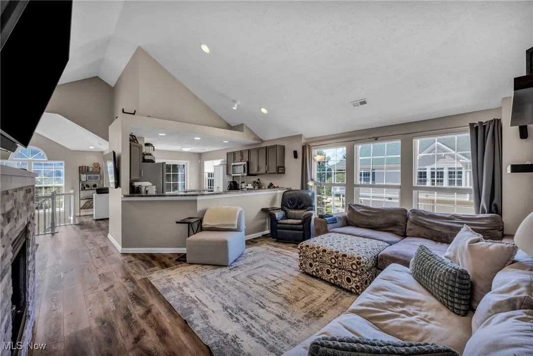 Living area featuring a stone fireplace, wood finished floors, healthy amount of natural light, high vaulted ceiling, and recessed lighting