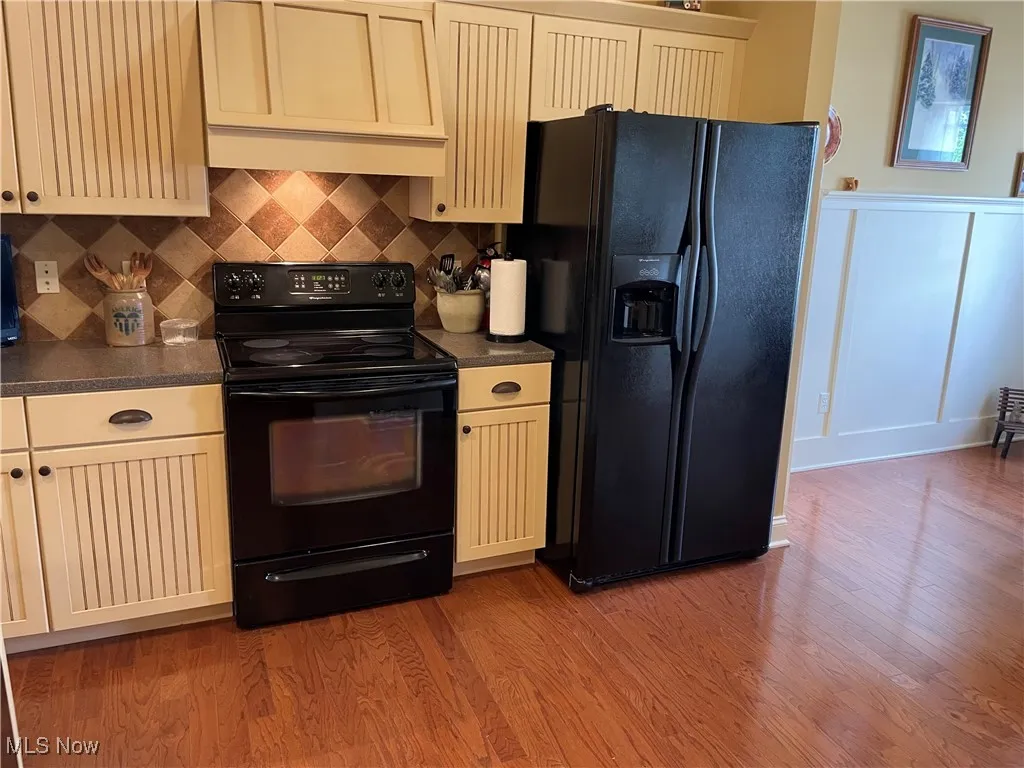 Kitchen featuring black appliances, cream cabinetry, light wood-style flooring, custom range hood, and decorative backsplash