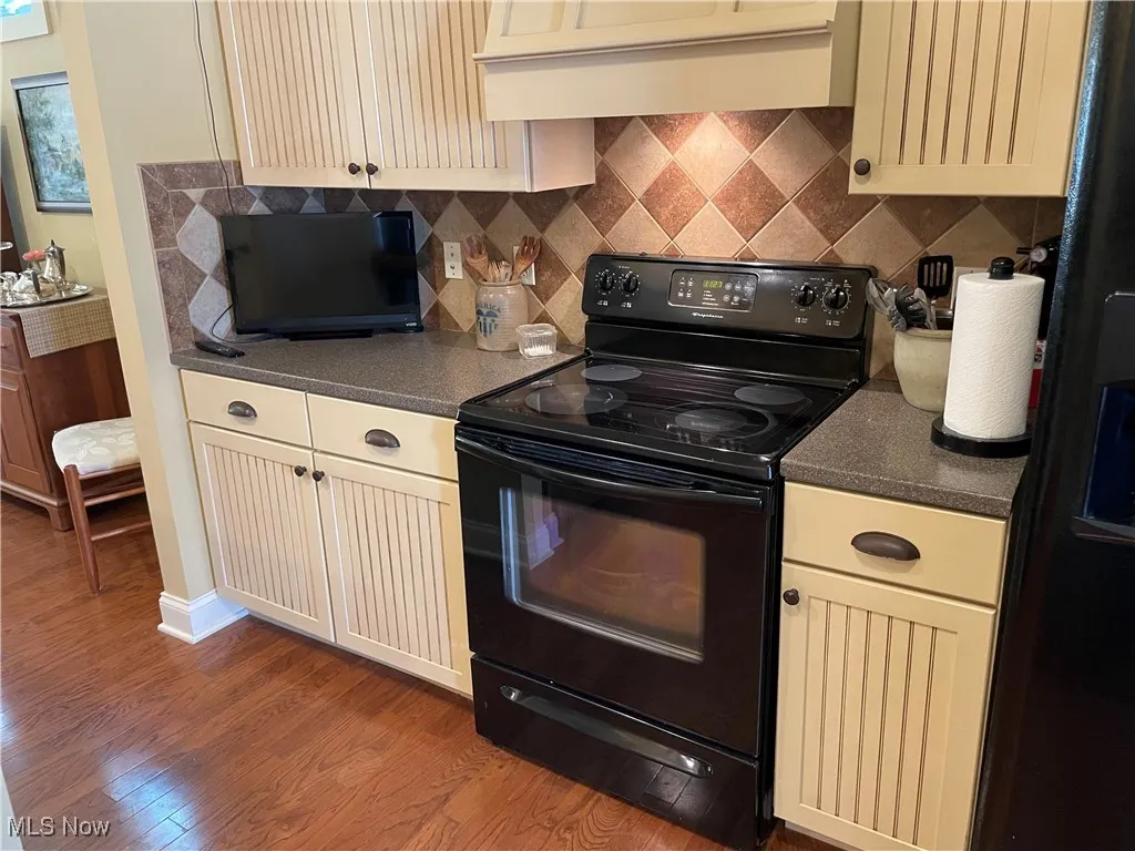 Kitchen featuring dark countertops, cream cabinetry, black appliances, extractor fan, and backsplash