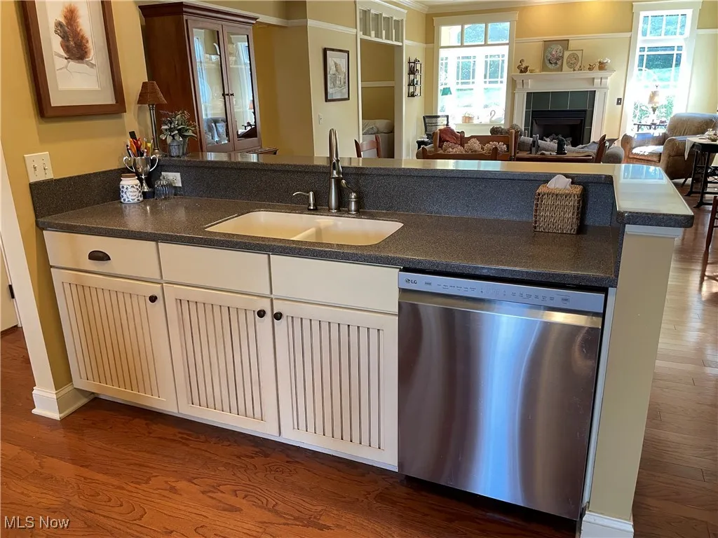 Kitchen with dark wood-style flooring, dishwasher, open floor plan, a tile fireplace, and dark stone counters