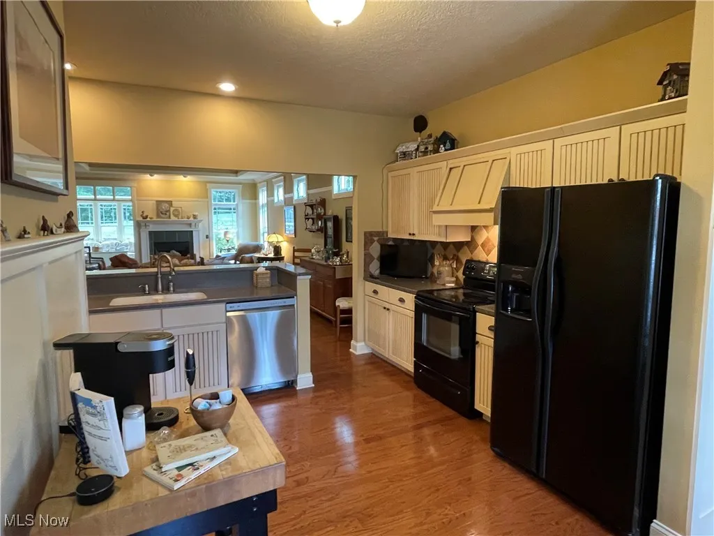 Kitchen featuring open floor plan, black appliances, dark countertops, custom range hood, and dark wood finished floors