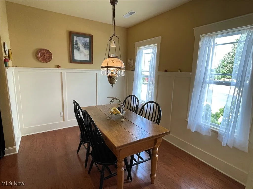 Dining room with a decorative wall, dark wood-type flooring, and wainscoting
