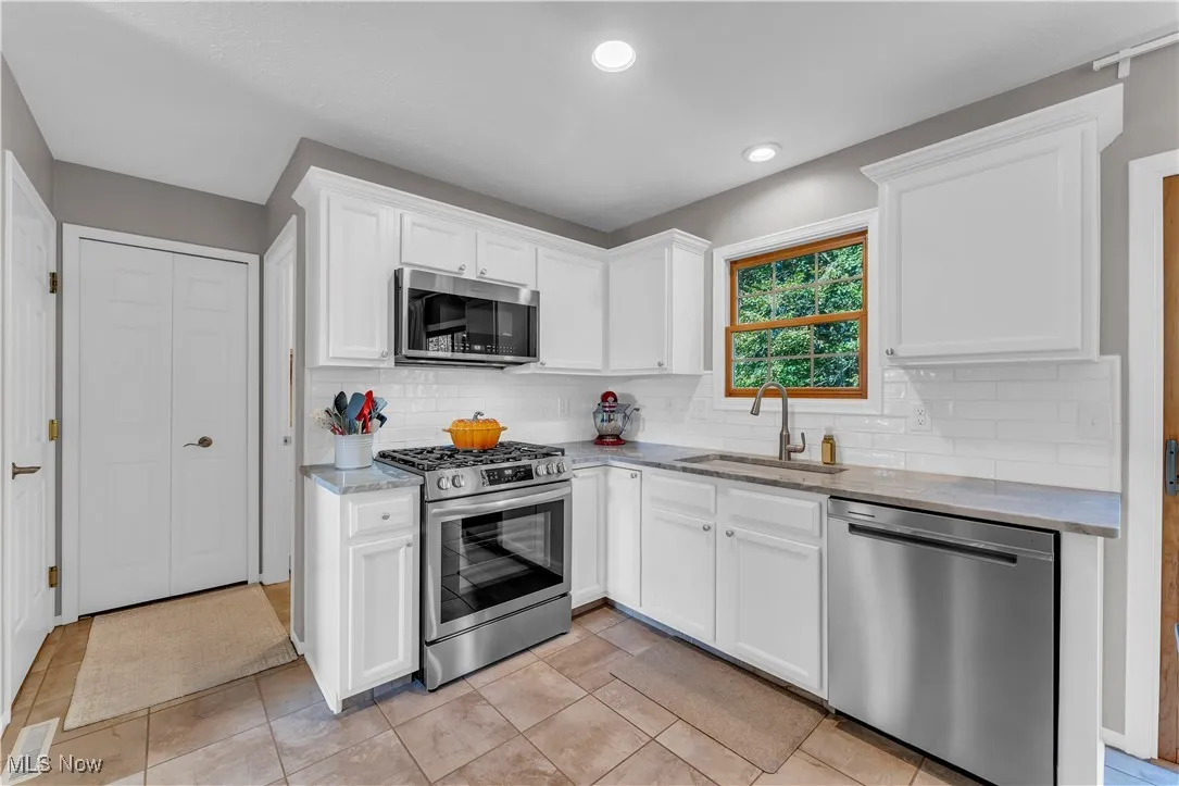Kitchen with appliances with stainless steel finishes, white cabinetry, light stone countertops, tasteful backsplash, and light tile patterned floors