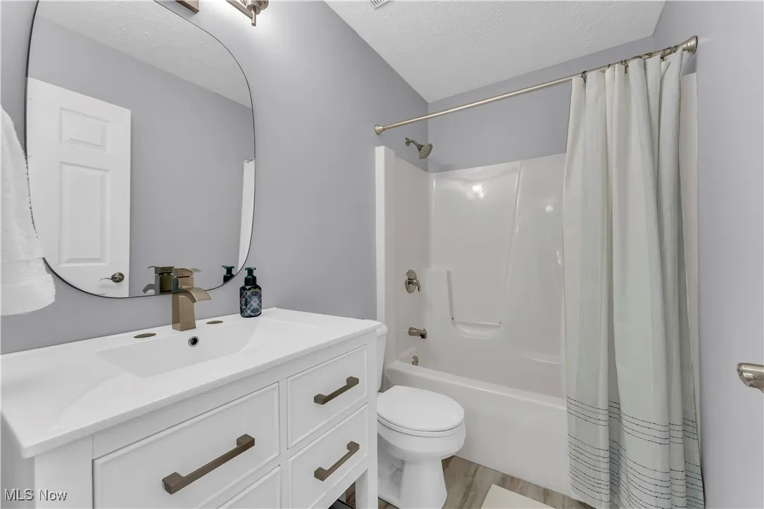 Bathroom featuring shower / bath combination with curtain, vanity, a textured ceiling, and light wood-type flooring