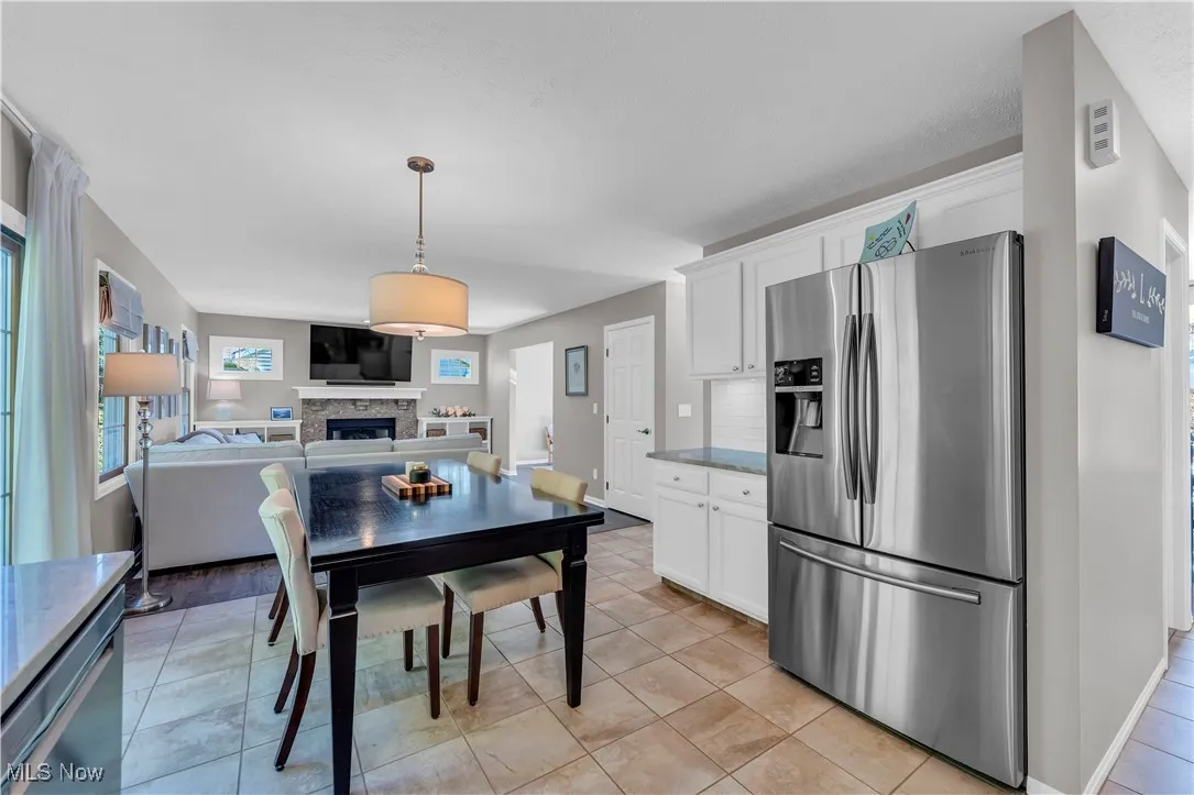 Kitchen featuring stainless steel fridge, white cabinets, open floor plan, a stone fireplace, and pendant lighting