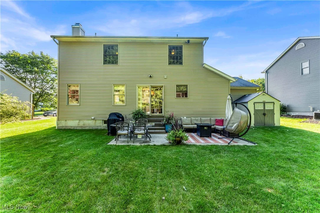 Rear view of property featuring a storage unit, a patio, a lawn, a chimney, and entry steps